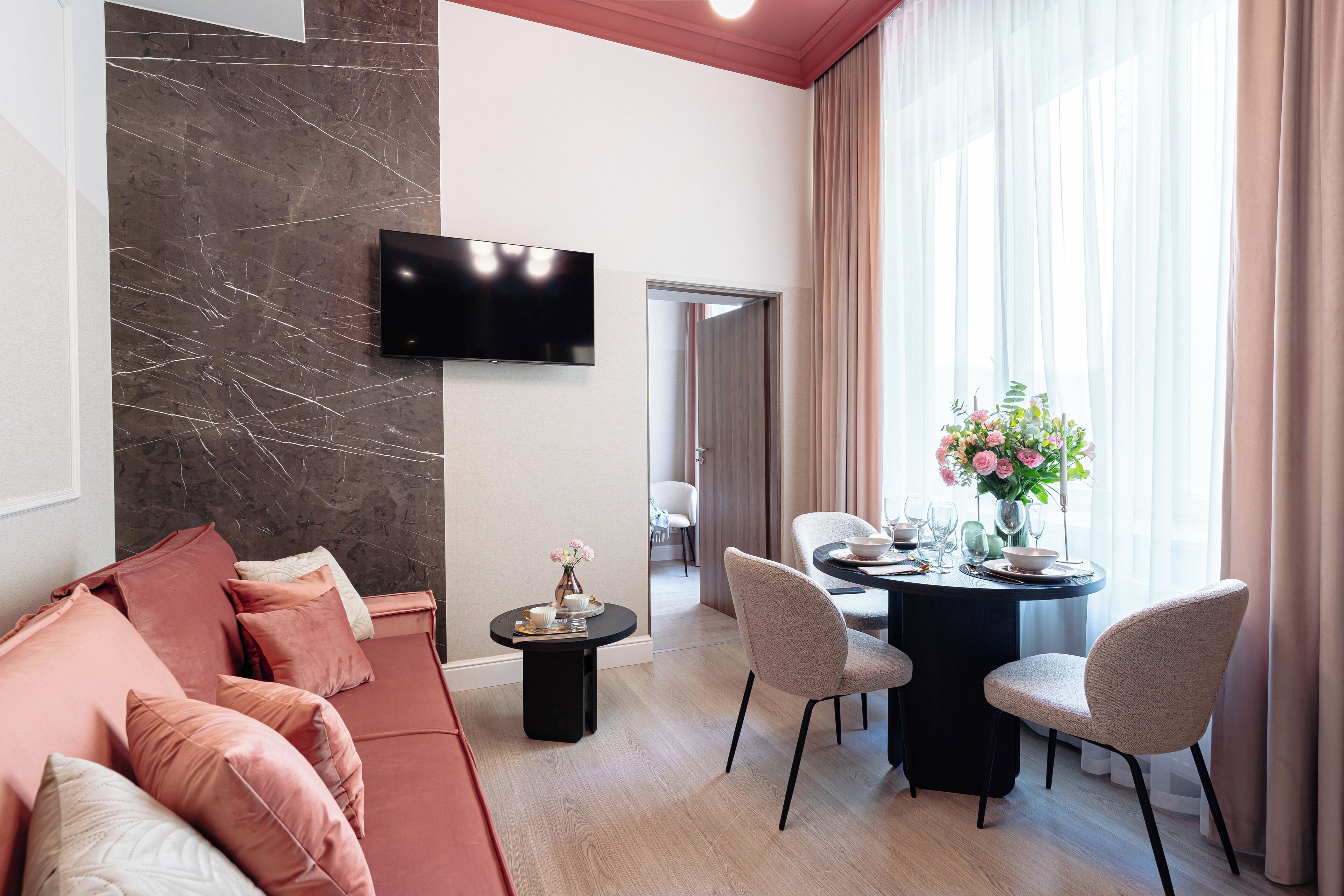 Un salon moderne comprenant un canapé, une table à manger avec des chaises, un téléviseur à écran plat fixé sur un mur en marbre, et donnant sur un couloir.