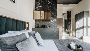 Een moderne slaapkamer met een groot bed, grijze beddengoed, een donker hoofdbord en een nachtkastje met een dienblad met spullen.
