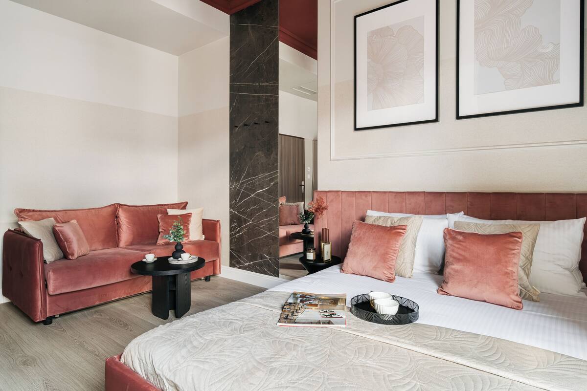Une chambre d’hôtel moderne avec un grand lit, un canapé rouge, une petite table d’appoint et des œuvres d’art encadrées accrochées au mur.