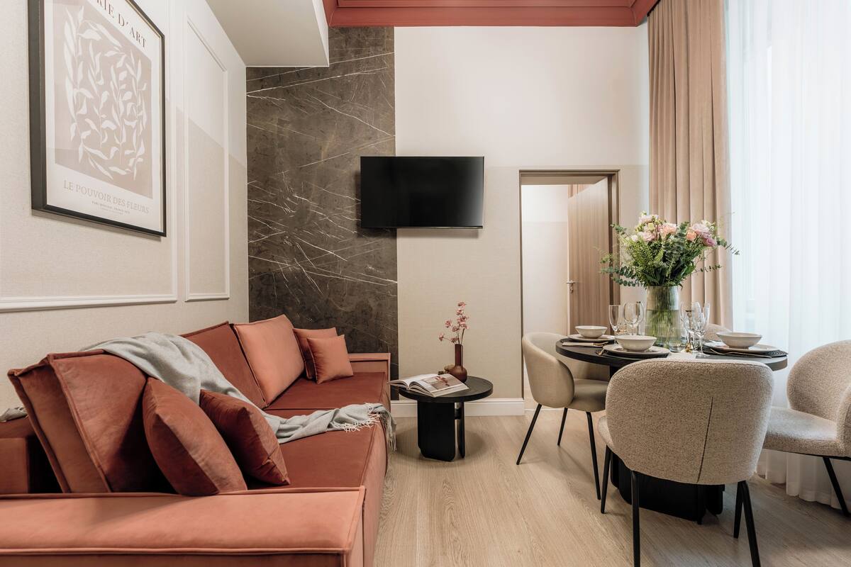 Un salon moderne comprenant un canapé, un téléviseur à écran plat, une table à manger avec des chaises et un vase rempli de fleurs.