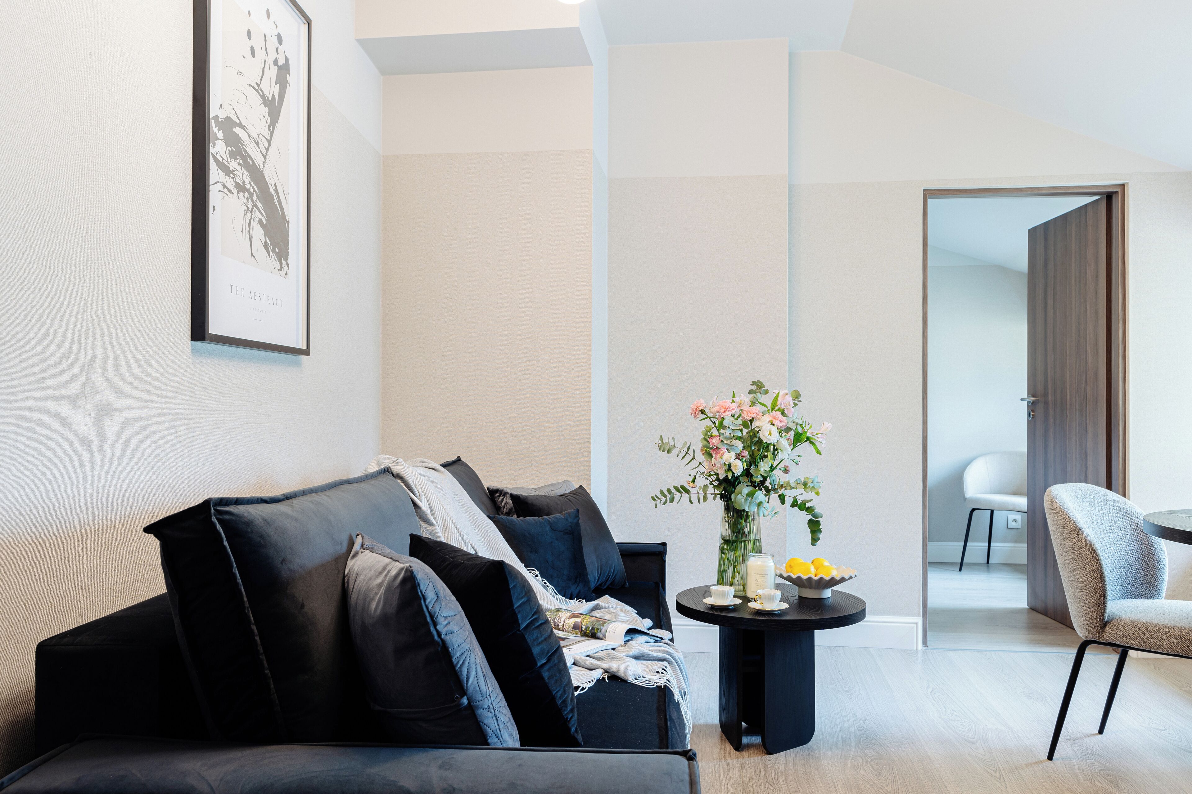 En moderne stue med en sort sofa, et rundt bord med en vase blomster og en lænestol.