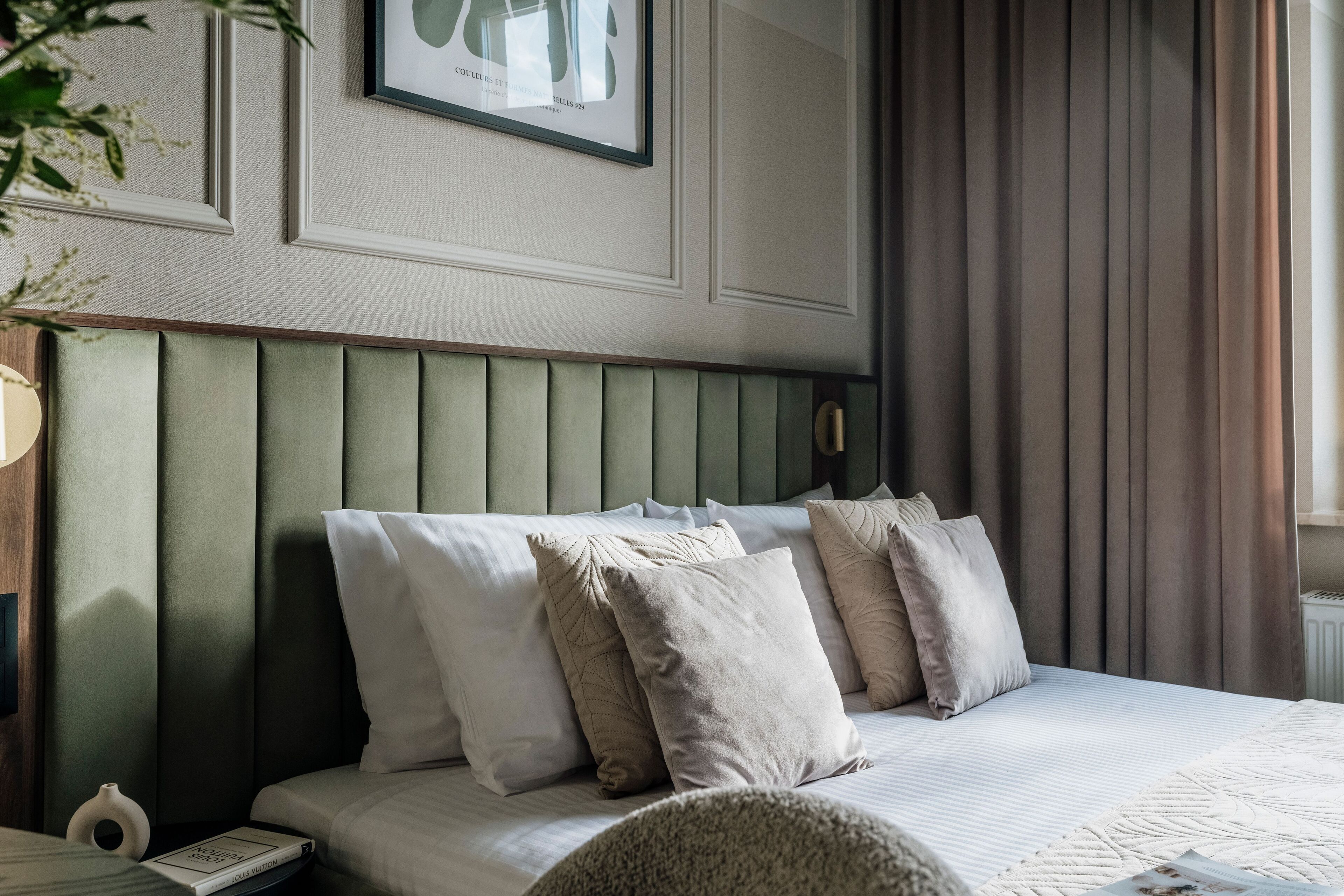 A neatly made bed with a green upholstered headboard, white bedding, and several pillows.