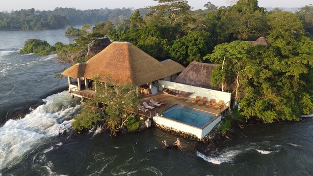 An overwater bungalow with a thatched roof, a pool, and lounge chairs.