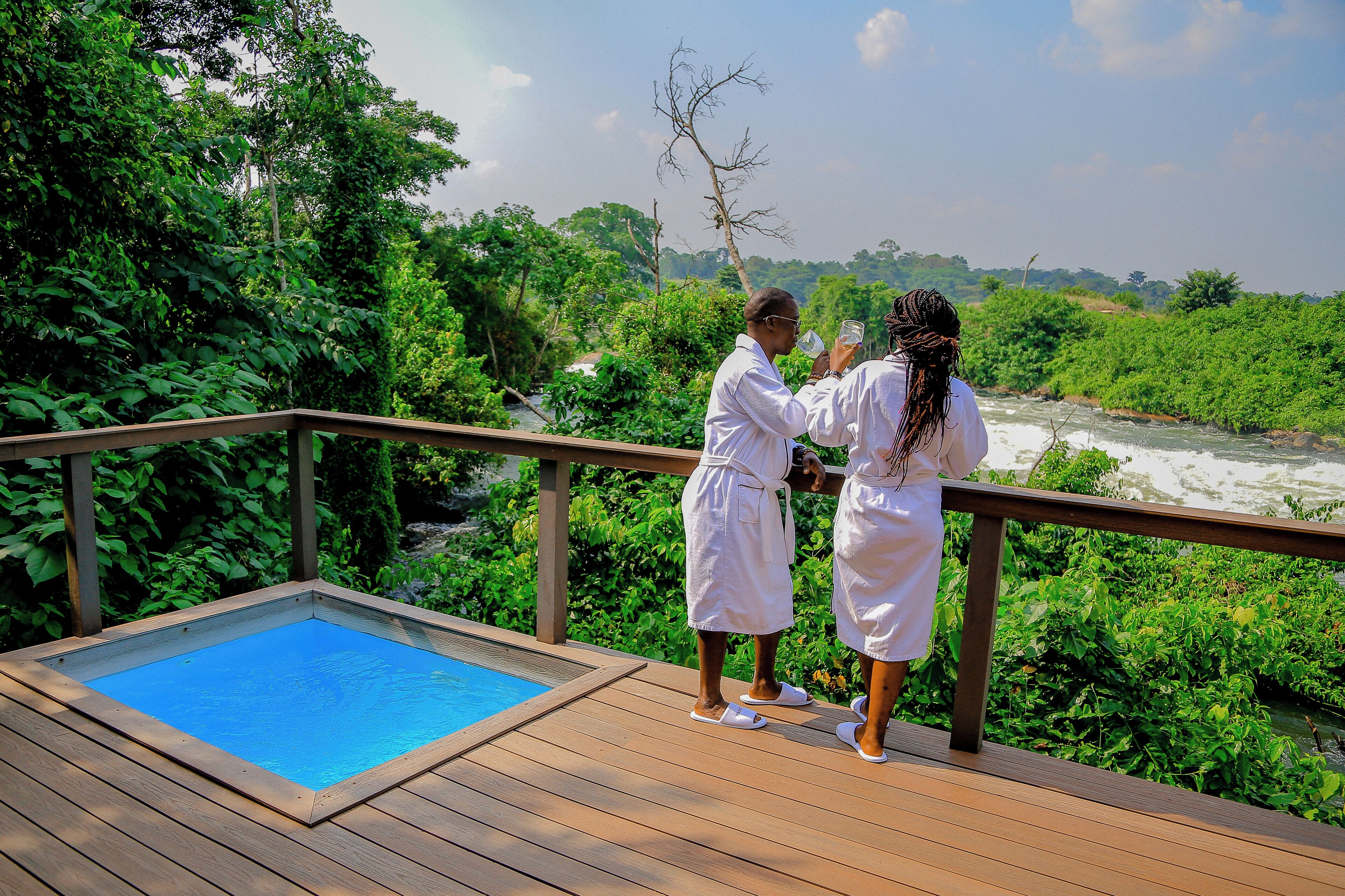 A wooden deck with a small pool and a railing overlooking a river and lush greenery.