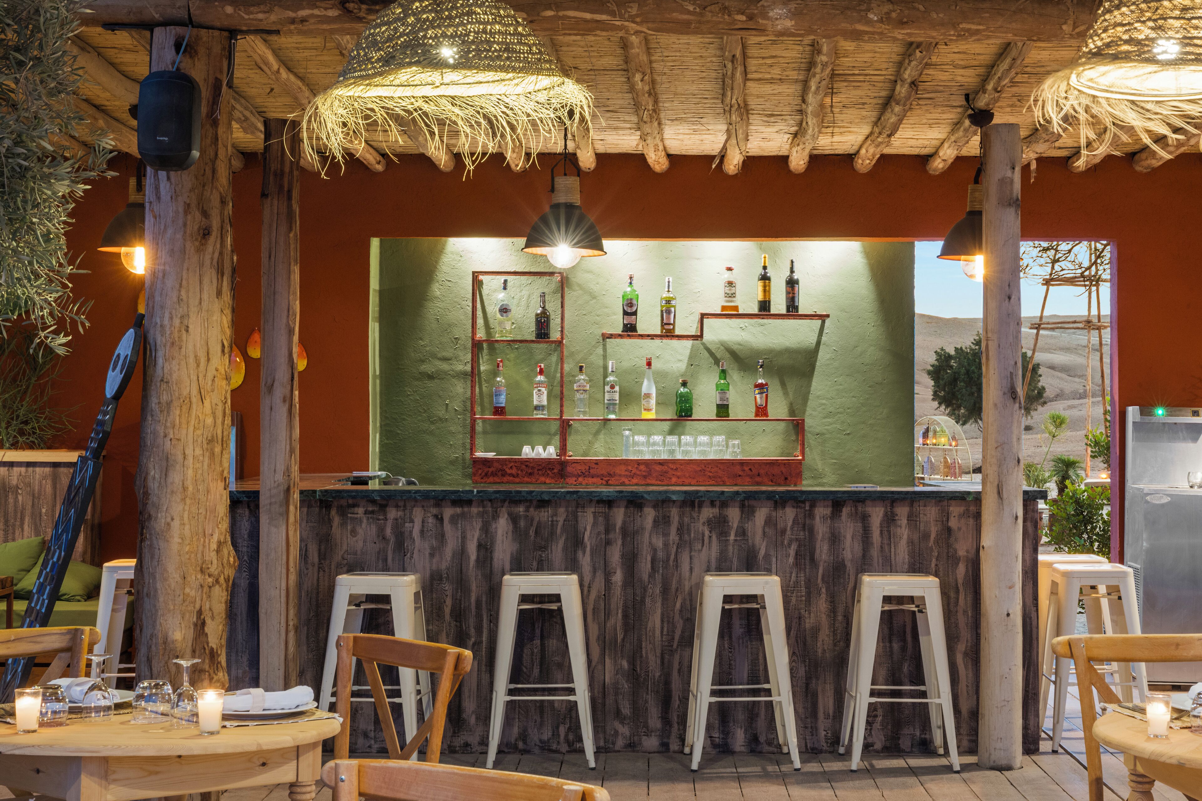 Un rústico espacio de bar con taburetes de madera, un fondo verde y una variedad de botellas.