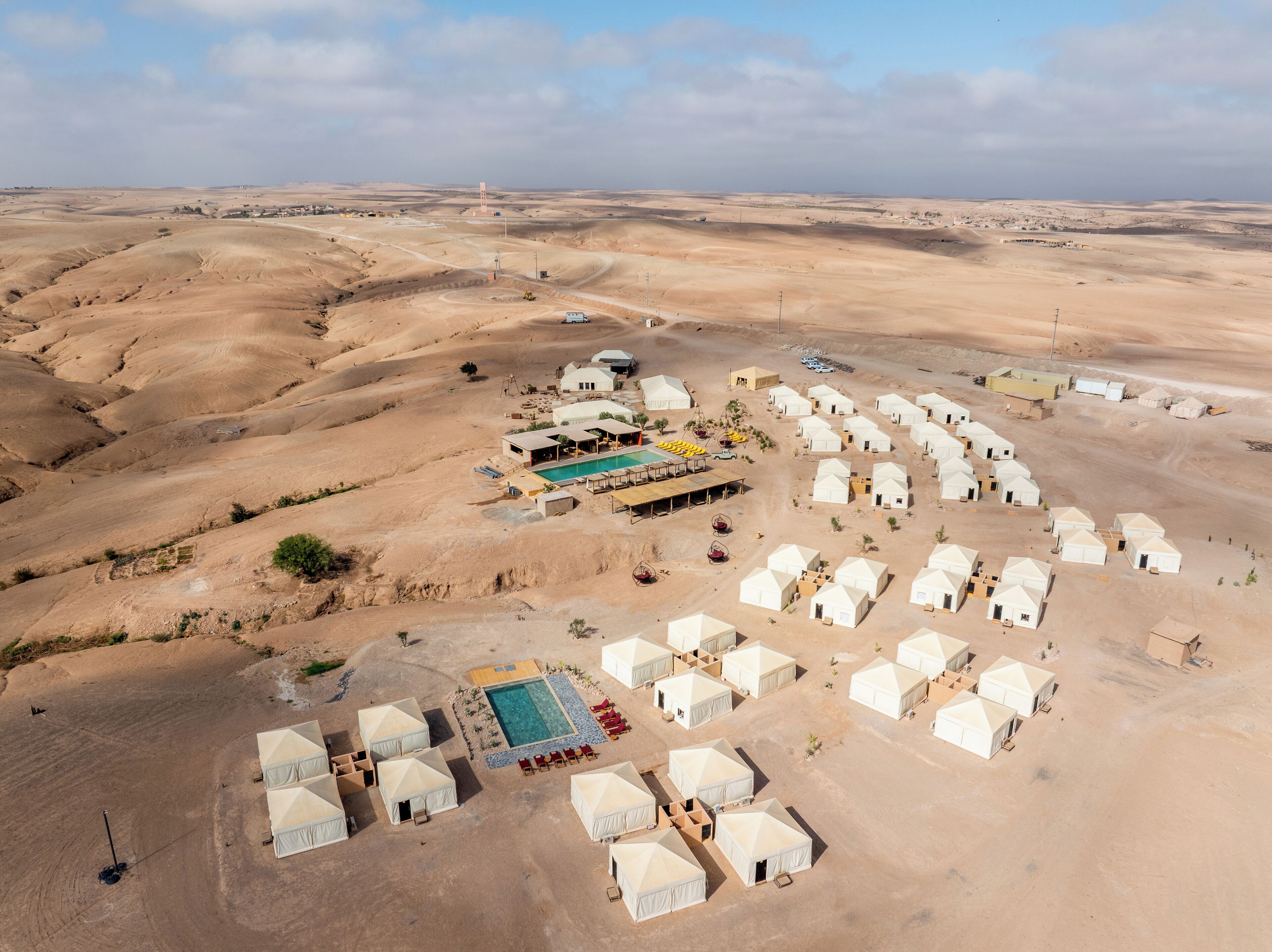 An aerial view of a desert resort with multiple yurts, a swimming pool, and a few buildings.