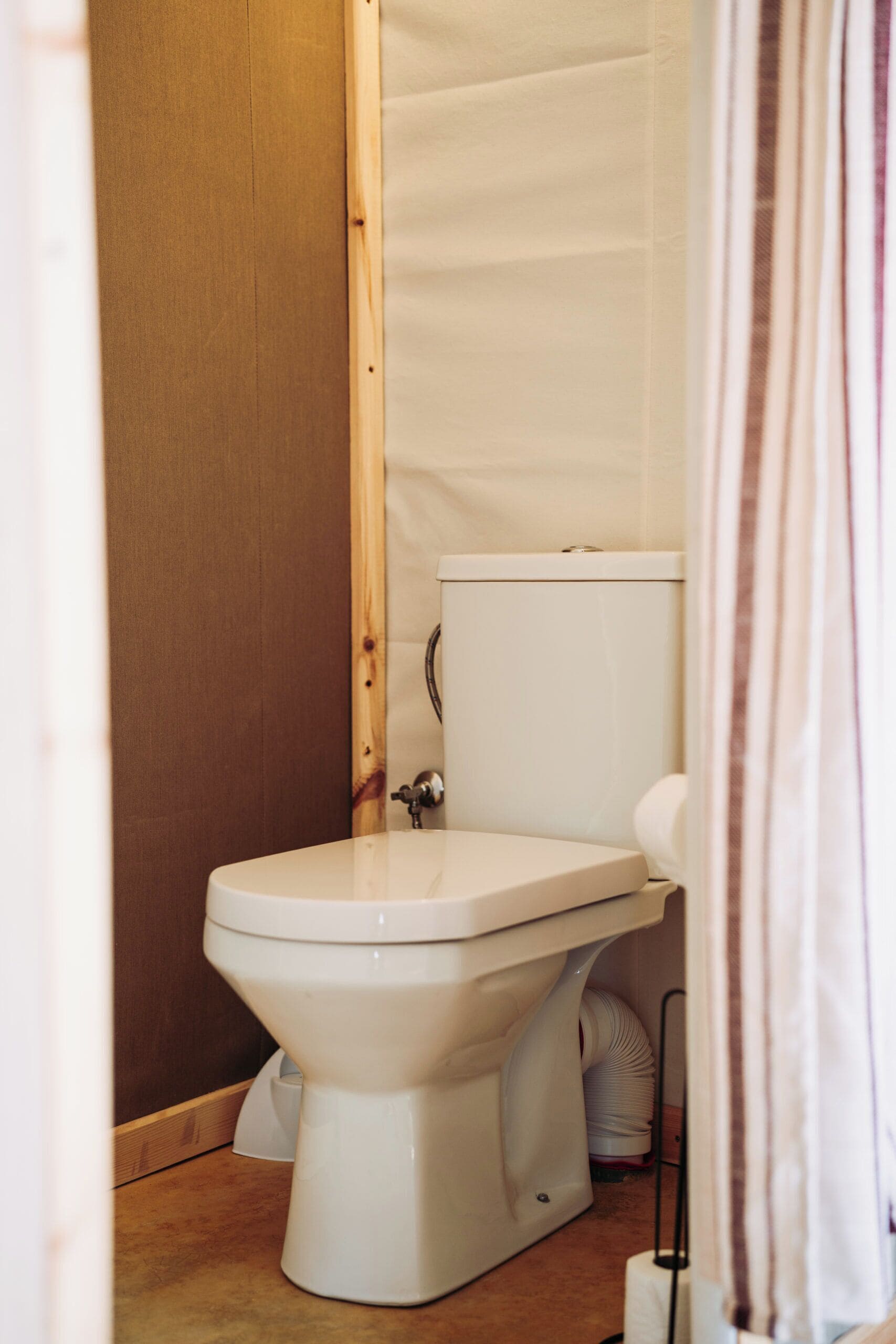 Un inodoro blanco estándar en un baño con un marco de puerta de madera y una cortina blanca parcialmente visible.