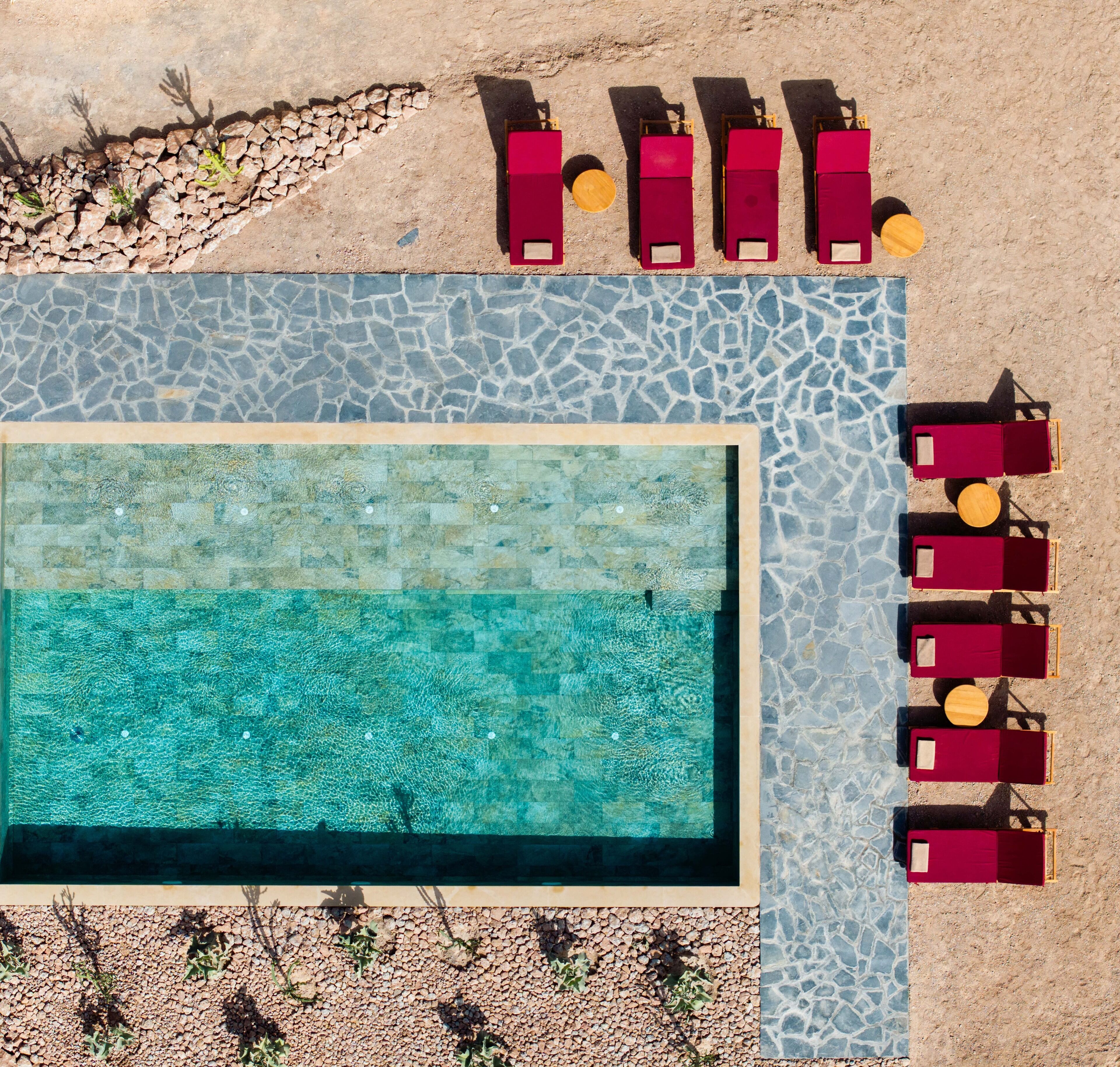 Vista aerea di una piscina con bordo piastrellato, circondata da sdraio e lettini.