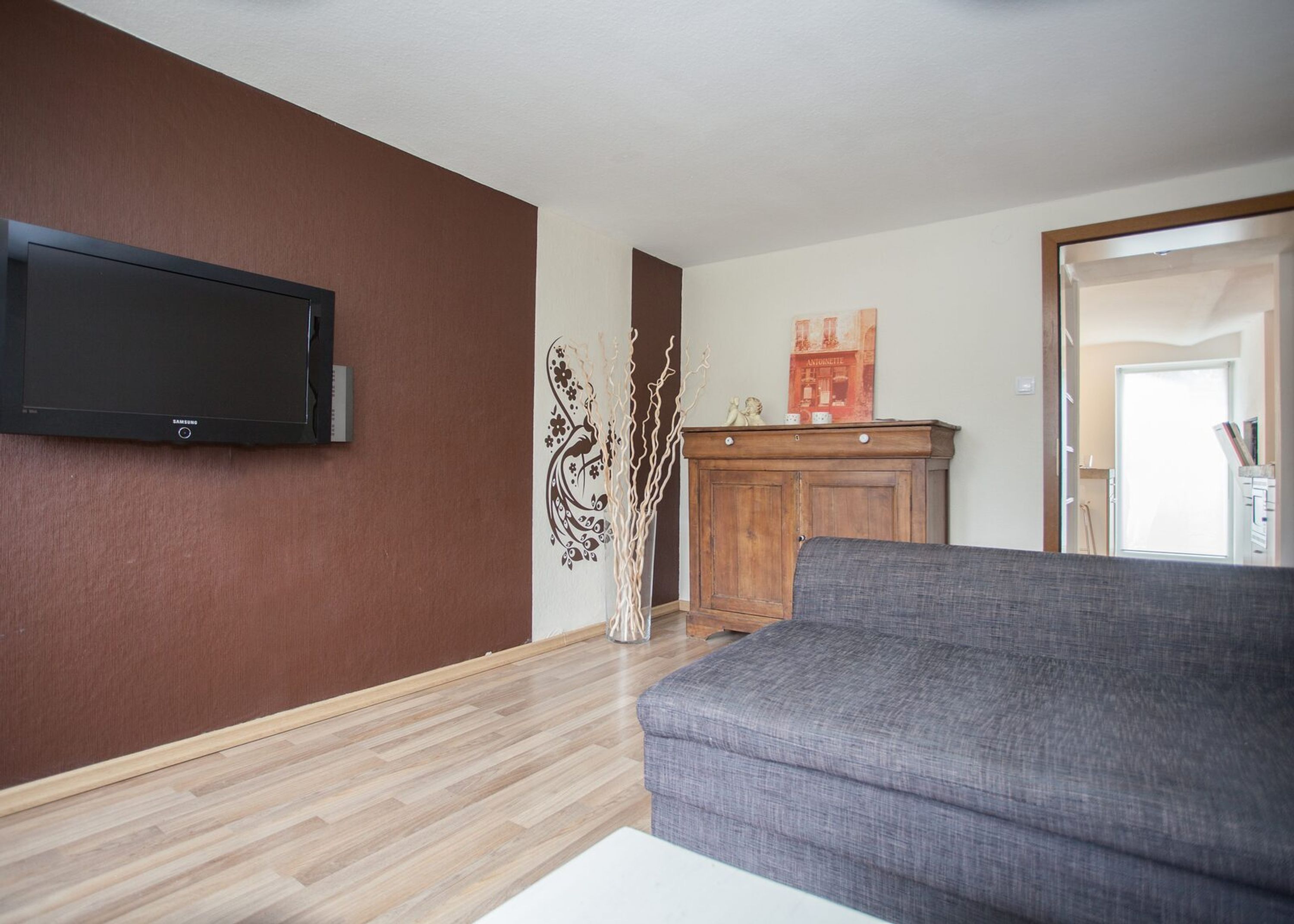 Un salon avec un téléviseur à écran plat fixé au mur, un meuble en bois et un canapé gris.