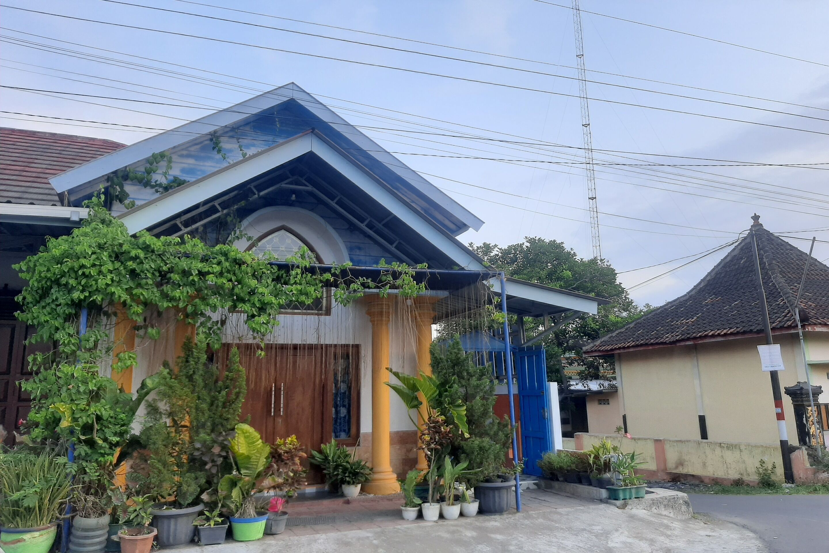 A house with a sloped roof, a large column, and various potted plants in the front yard.