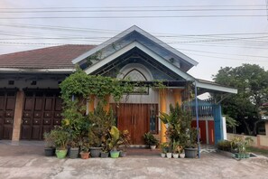 A house with a wooden front door, potted plants, and a blue structure to the right. - Hotel O Griya Rizky Homestay Syariah (Ngemplak)