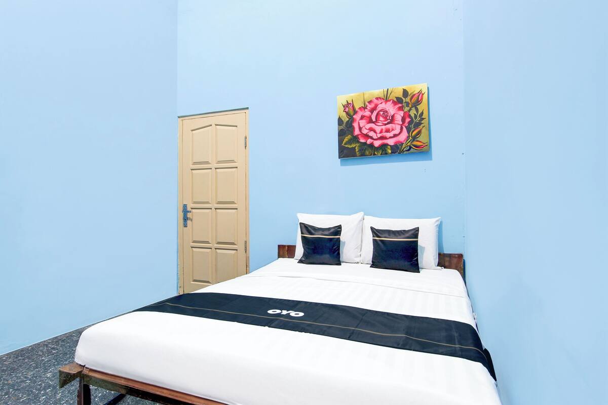 A single bed with a black and white bedspread, a painting of a rose on the wall, and a wooden door.