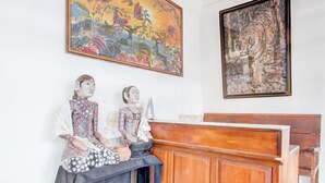 A room with two traditional statues, a wooden reception desk, and two paintings on the wall.