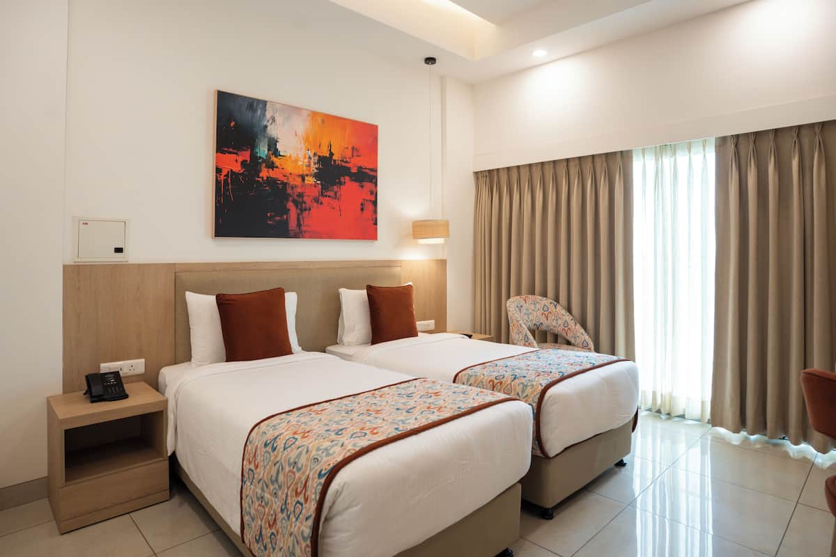 A hotel room with two beds, a nightstand with a phone, a painting on the wall, and a window with curtains.