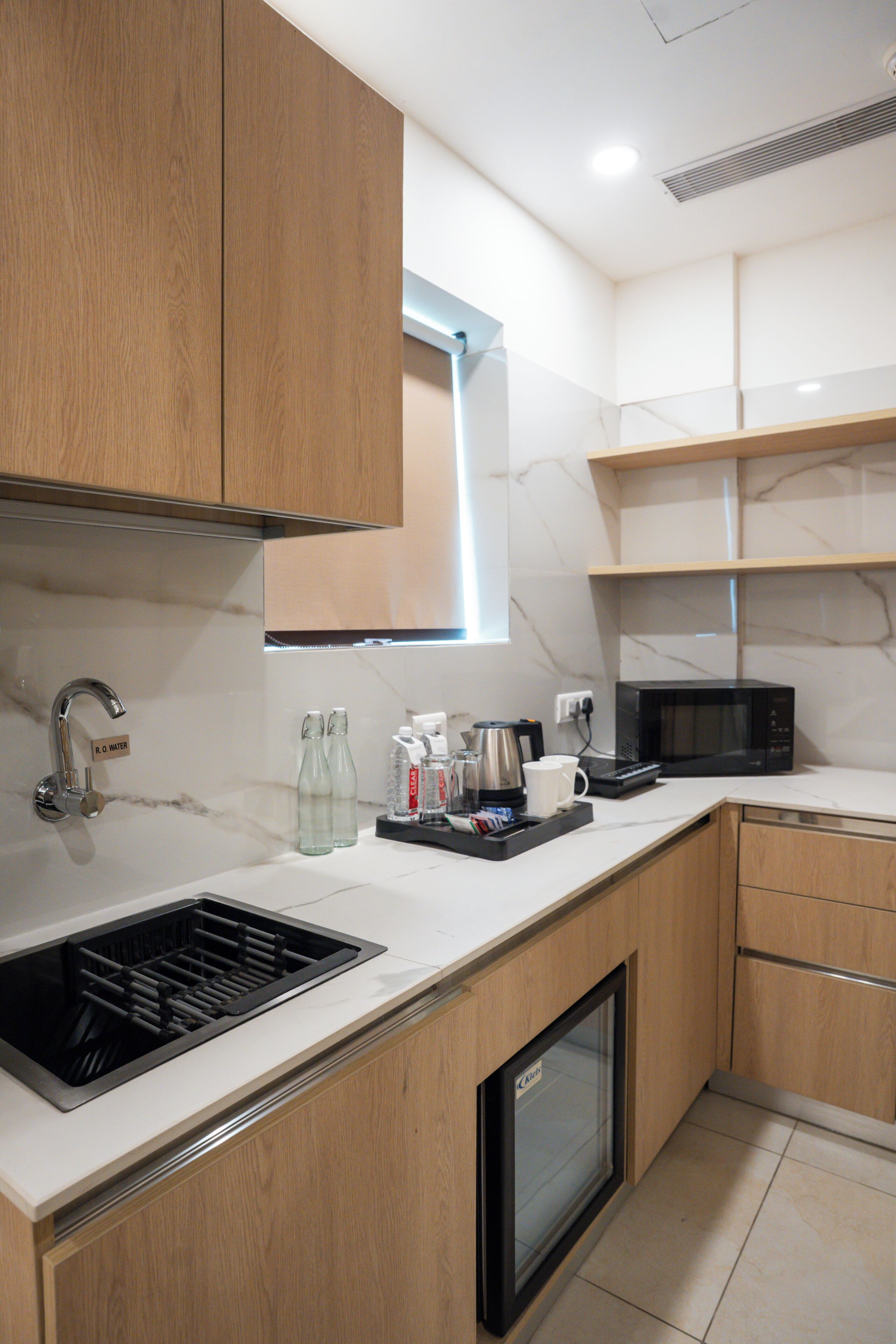 A modern kitchen with wooden cabinets, a built-in microwave, a coffee maker, and a small refrigerator.