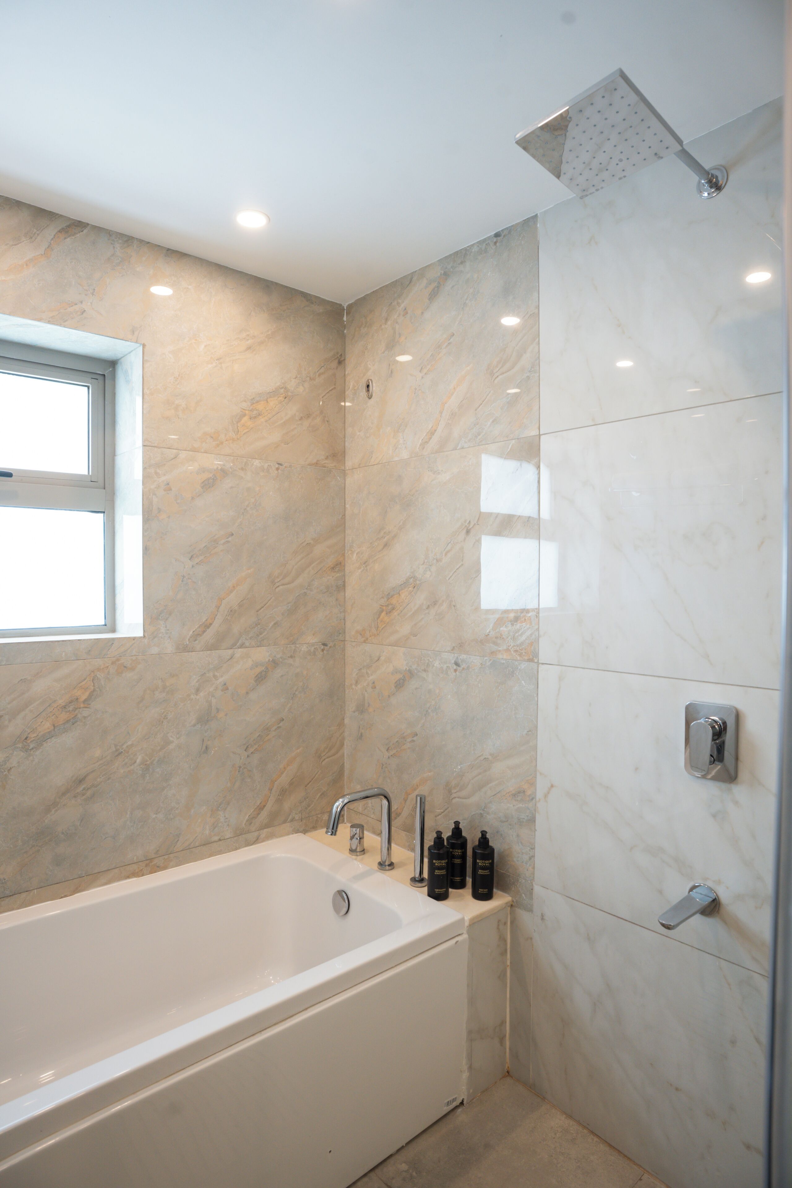 A modern bathroom with a bathtub, a shower, and marble walls.