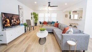 A modern living room with a grey sofa, a white entertainment unit, and a dining area with a table and chairs.