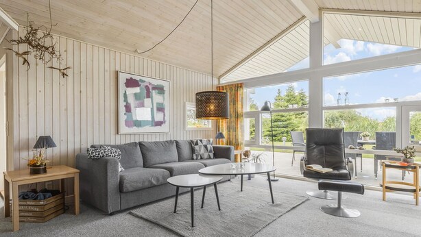 A modern living room with a grey sofa, a coffee table, and a black leather chair. There is a large window providing a view of the outdoors. - Stunning home in Otterup with sauna (Otterup)