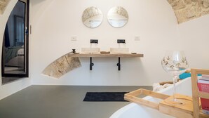 Ein modernes Badezimmer mit einem Steinbogen, zwei runden Spiegeln, einer Holzausstattung mit Waschbecken und einem Weinglas auf einem Tablett.