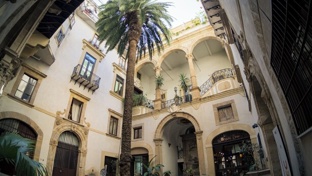 Ein Innenhof mit einer Palme, Bögen und einem Gebäude, in dem sich das Geschäft 