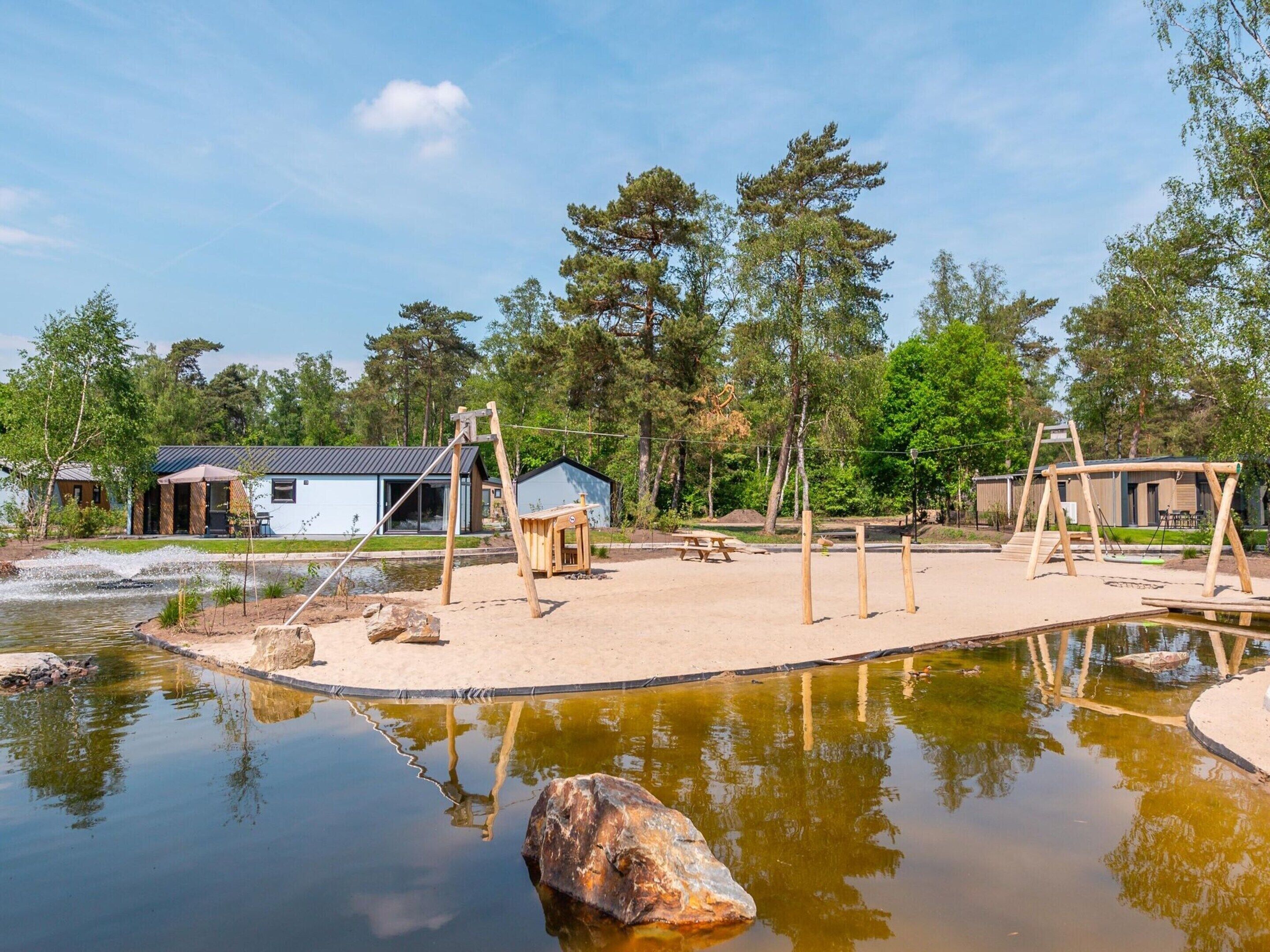 Een park aan het meer met houten schommels, een picknicktafel en een klein vakantiehuis.