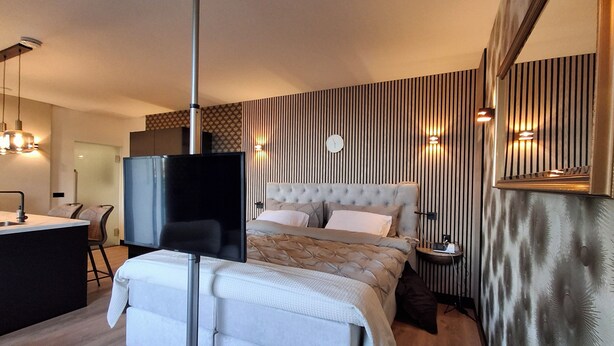 Ein modernes Hotelzimmer mit einem großen Bett, einem Flachbildfernseher, einem Schreibtisch und einem im Hintergrund sichtbaren Badezimmer.