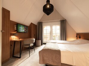 Ein Hotelzimmer mit Bett, Schreibtisch, Stuhl, Fernseher und einem großen Fenster mit Vorhängen.