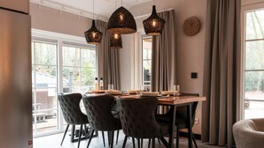A modern dining area with a wooden table, four upholstered chairs, and three hanging pendant lights. - Luxe Villa met Wellness en Domotica (Soest)