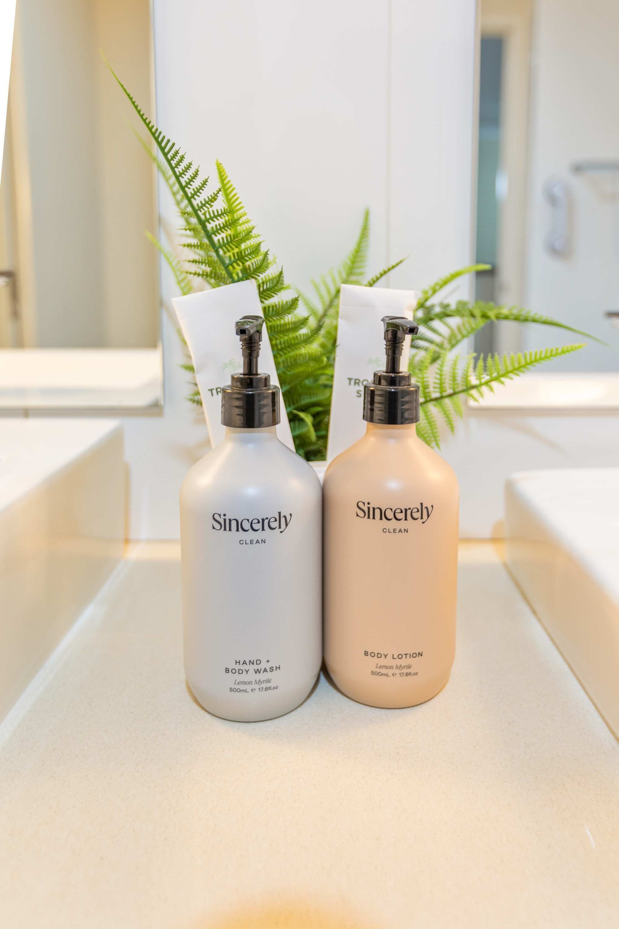 Twee flessen Sincerely Clean douchegel en lotion op een badkamermeubel met een varen.