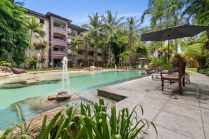 A resort pool area with a fountain, surrounded by palm trees and a multi-story building with balconies. - Lux Apartment Cairns - 9 Pools BBQ Gym (Westcourt)