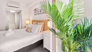 A hotel room with a bed, bedside table, and a large potted plant. - Lux Apartment Cairns - 9 Pools BBQ Gym (Westcourt)