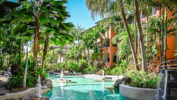 Piscina de resort con agua cristalina, rodeada de palmeras y un edificio con balcones.