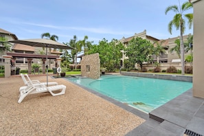 A pool area with lounge chairs, a stone feature, and a covered seating area.