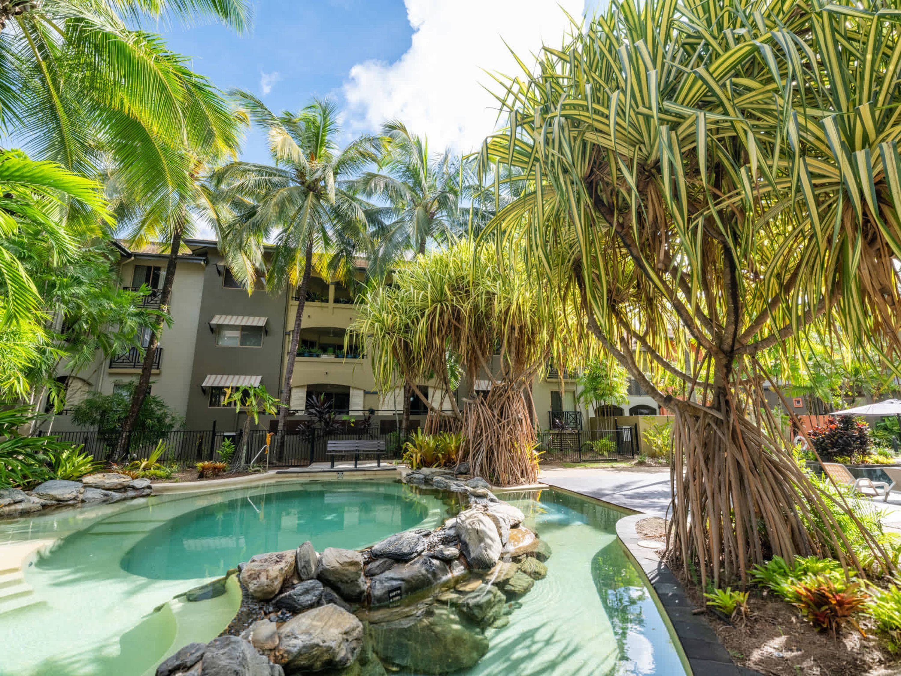 Uma piscina rodeada por plantas tropicais e um edifício com varandas.