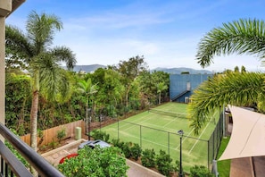 A tennis court with a surrounding fence, trees, and a building in the background.