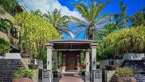 Der Eingang eines tropischen Resorts mit überdachtem Gang, Palmen und großen Pflanzgefäßen.