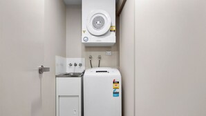 Une petite buanderie comprenant un lave-linge, un sèche-linge, un petit meuble de rangement et un radiateur fixé au mur.