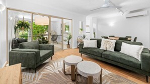 A modern living room with a green sofa, two round coffee tables, and a large window with a view of greenery. - The Nest Cairns - 4 Pools BBQ Resort (Cairns North)