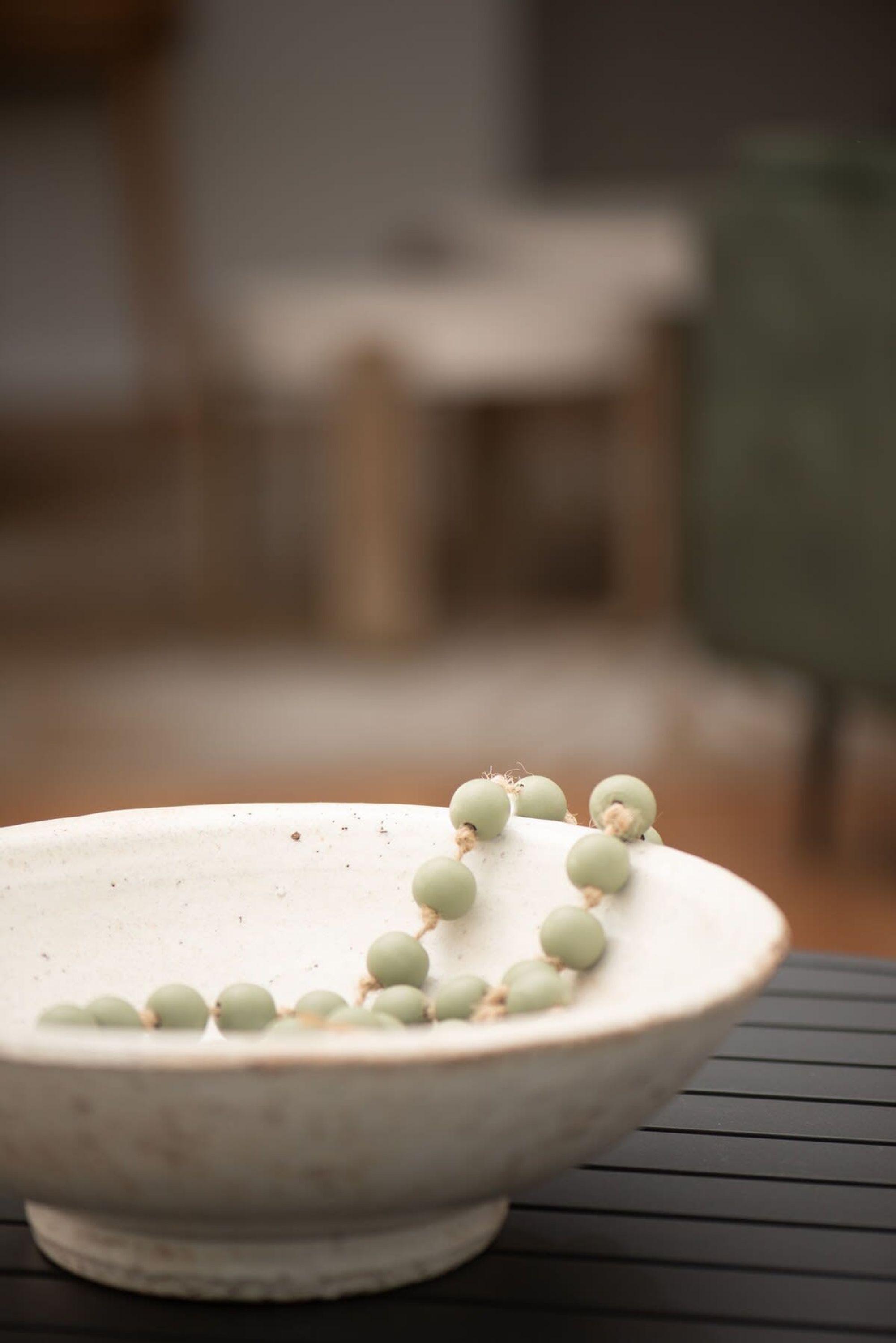 A white ceramic bowl with green beads on a black table.