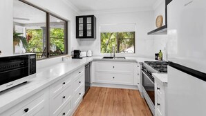 A modern kitchen with white cabinetry, a built-in oven, and a large window offering a view of greenery. - The Nest Cairns - 4 Pools BBQ Resort (Cairns North)