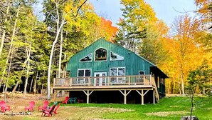 A large, green wooden cabin with a balcony, surrounded by trees with autumn foliage. - Moose Lane  *Waterfront*ATV/Snowmobile Access* (Greenville)