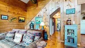 A cozy cabin interior with a wooden interior, a couch with patterned cushions, a lamp, and a bookshelf. - Moose Lane  *Waterfront*ATV/Snowmobile Access* (Greenville)