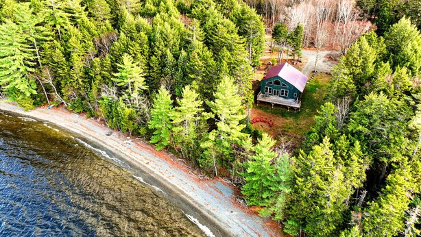 An aerial view of a cabin surrounded by dense forest, near a rocky shoreline. - Moose Lane  *Waterfront*ATV/Snowmobile Access* (Greenville)