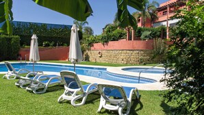 A pool area with lounge chairs and umbrellas, surrounded by greenery and a stone wall. - Casa La Buganvilla del Chaparral (Marbella)