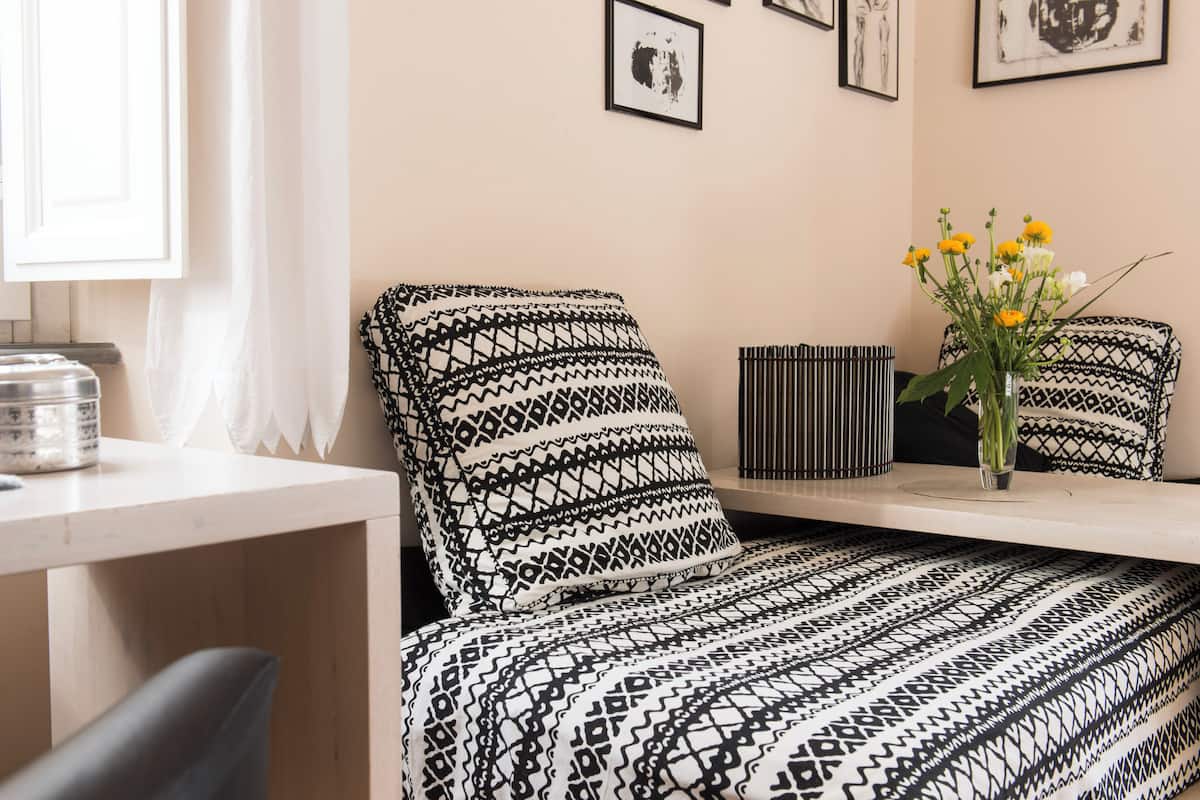 A room with a bed, a desk, and a chair. There is a vase with flowers on the desk.