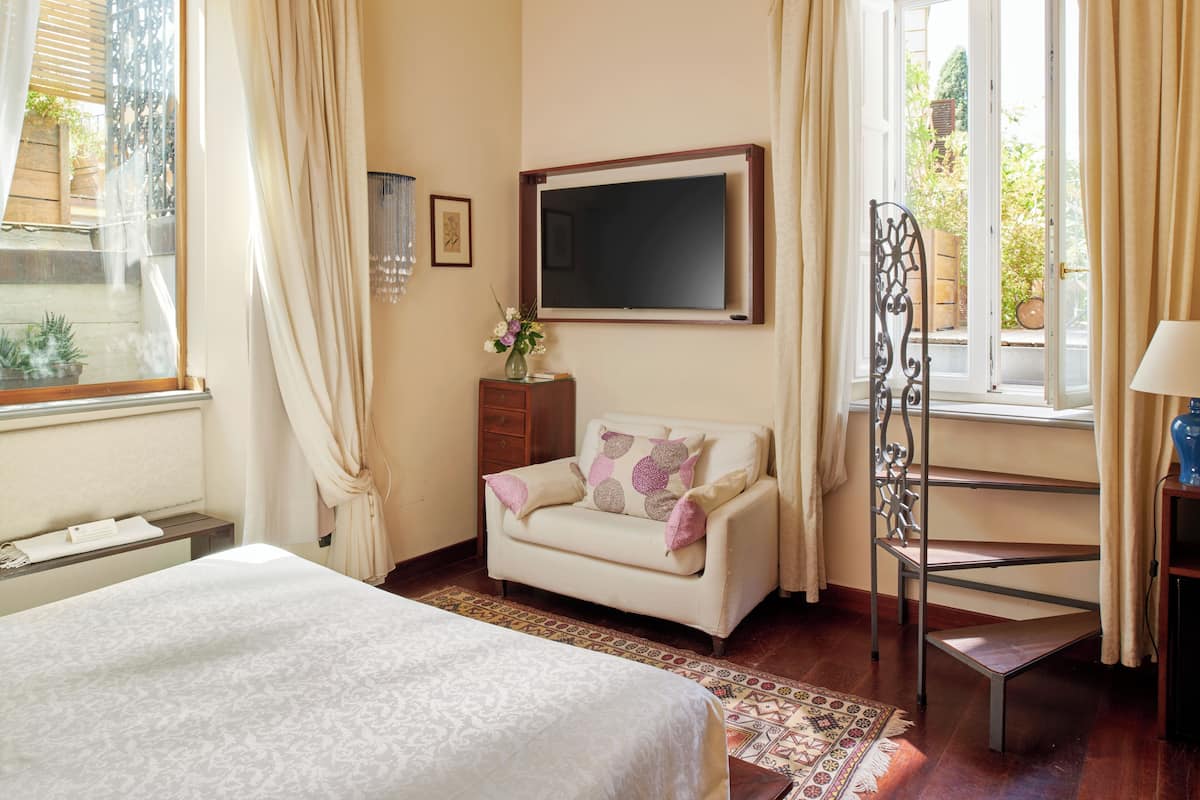 A hotel room with a bed, a sofa, a TV, a small table, and a window with curtains.