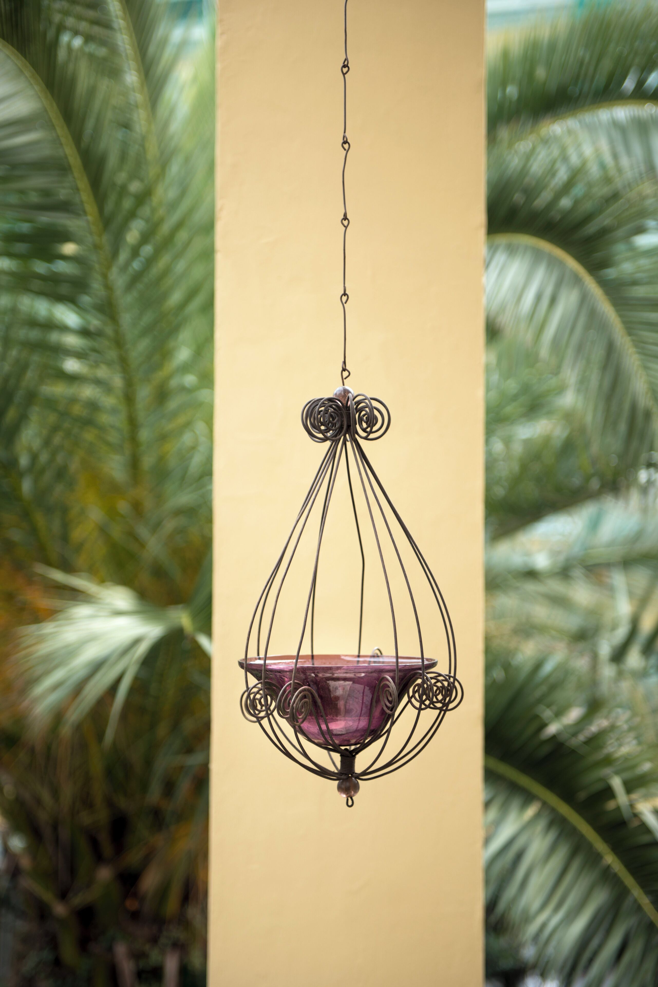 A hanging light fixture with a purple glass shade, surrounded by a metal frame, against a beige wall.