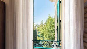 A window with a green metal railing, white curtains, and a view of trees and buildings. - Palm Gallery Hotel (Rome)