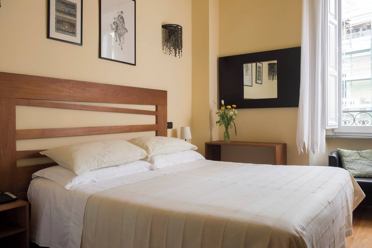 A neatly made bed with a wooden headboard, a bedside table with a lamp, and a wall-mounted mirror.