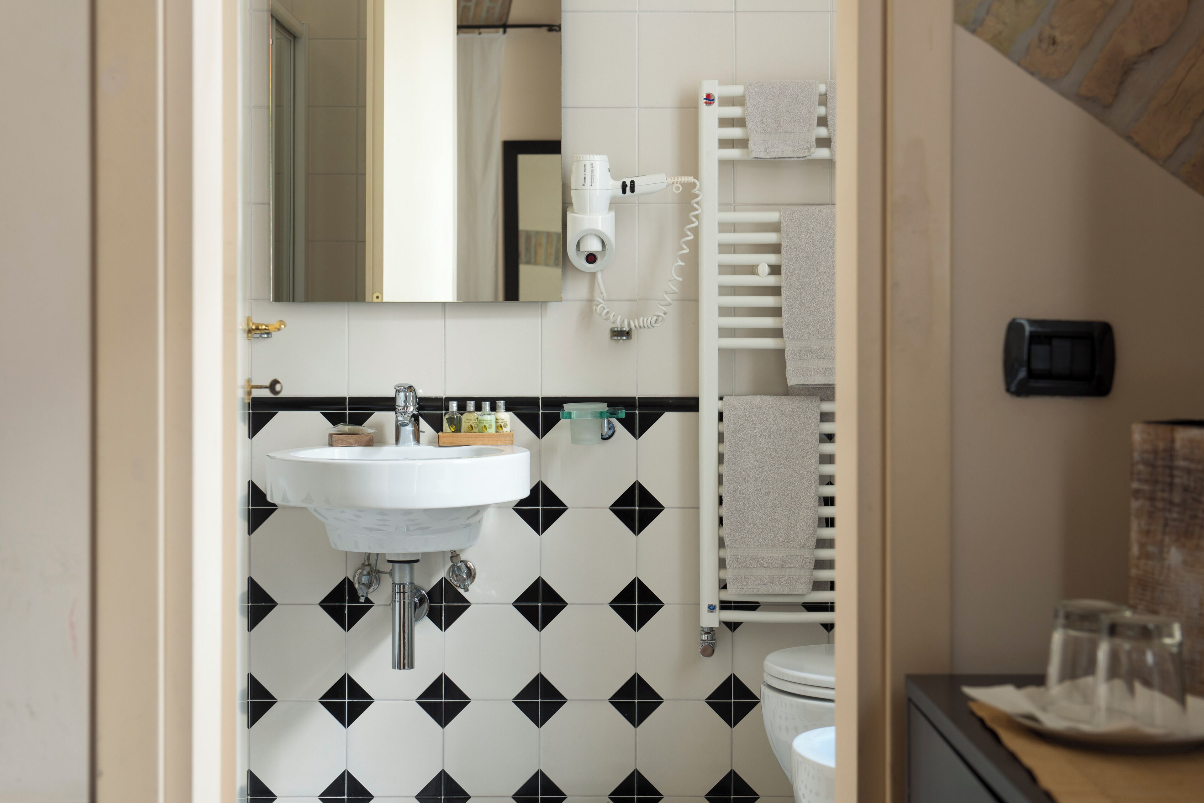 A bathroom with a white sink, black and white patterned tiles, a towel rack, and a hairdryer mounted on the wall.